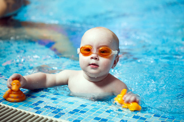 Ребенок плавает в бассейне. Маленький мальчик учится плавать в бассейне
 - Фото, изображение