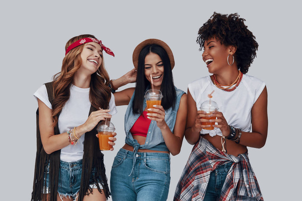 Three attractive young women drinking refreshing cocktails and smiling while standing against grey background - Valokuva, kuva
