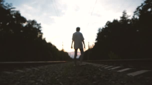 Genç bir defodaklanmış adam gün batımında bir demiryolu hattının ortasında yürüyor - Video, Çekim
