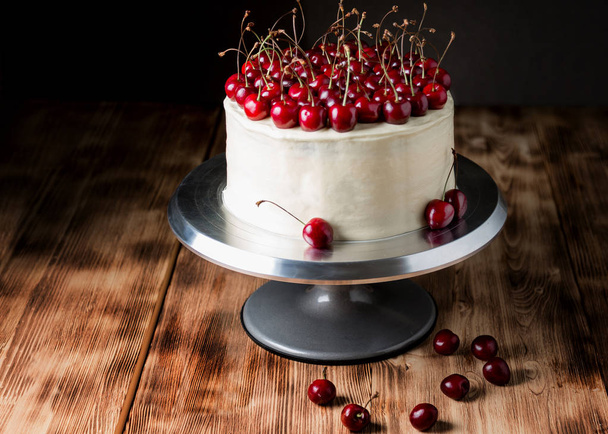 Торт "Красный бархат", очень красивый, со сладкой вишней, на темном фоне и светлом деревянном столе
 - Фото, изображение