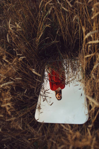 Krásná žena v červených šatech v zrcadlovém zrcadle na poli. - Fotografie, Obrázek