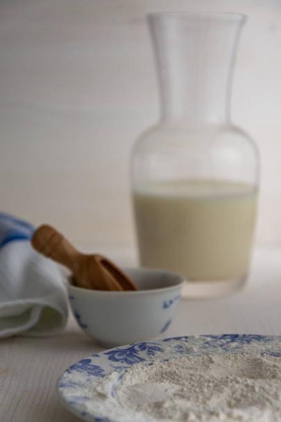 Widok składników do ciasta, mąki z butelką z mlekiem i szmatki na białym tle drewnianym - Zdjęcie, obraz