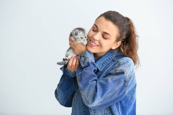 Beautiful young woman with cute little kitten on light background - Foto, afbeelding