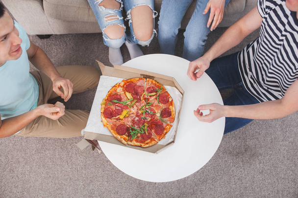 Молодые люди едят пиццу вид сверху. Группа друзей обедает в помещении. Смешные друзья вместе. - Фото, изображение
