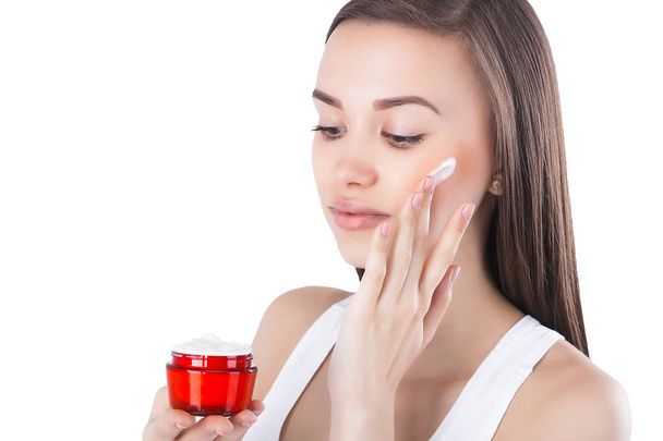 Retrato de close-up de jovem mulher atraente aplicando creme facial. Mulher segurando um frasco com creme hidratante para o rosto
. - Foto, Imagem