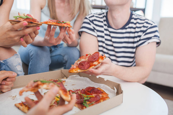Οι νέοι τρώνε πίτσα. Μια ομάδα φίλων που τρώνε σε εσωτερικούς χώρους. Αστείοι φίλοι μαζί. - Φωτογραφία, εικόνα