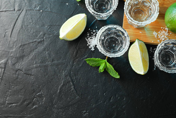 Tequila shots with salt, lime slices and mint on black table - 写真・画像