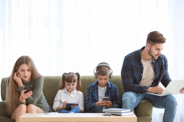 Familia adicta a las tecnologías modernas con dispositivos sentados en el sofá en casa
 - Foto, imagen