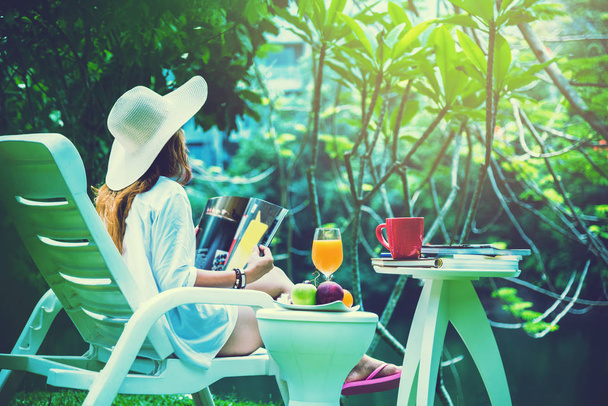Donna asiatica Seduto rilassarsi. Leggi riviste e bevi succo di frutta. in giardino
 - Foto, immagini