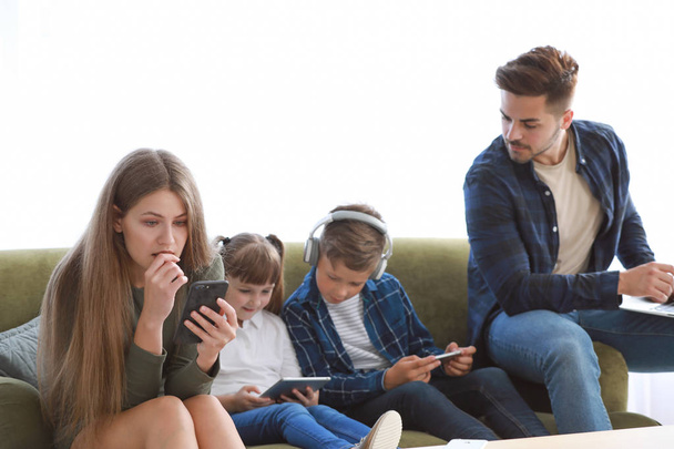 自宅のソファに座っているデバイスを持つ現代の技術に夢中の家族 - 写真・画像