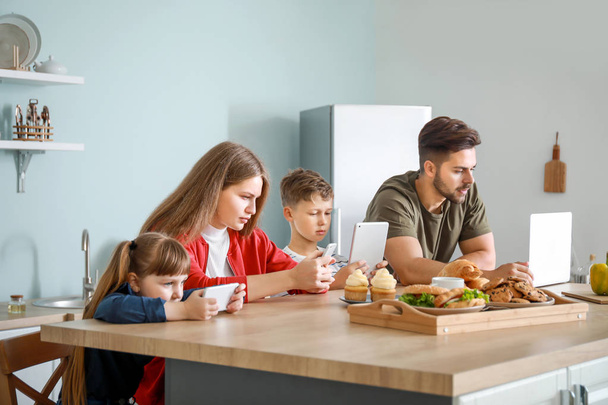 Família com dependência de tecnologias modernas sentada à mesa na cozinha
 - Foto, Imagem