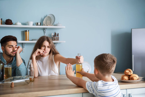 Matka oferuje alkohol do małego syna w kuchni w domu. Koncepcja uzależnienia - Zdjęcie, obraz