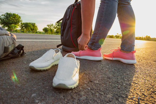 La mujer dejó los zapatos de trabajo y usó zapatillas de deporte en la carretera con la luz dorada del sol. Concepto de vacaciones y viajes
 - Foto, Imagen
