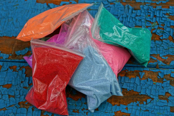un ramo de pequeñas bolsas de plástico de arena de color sobre una mesa azul desgastada
 - Foto, Imagen