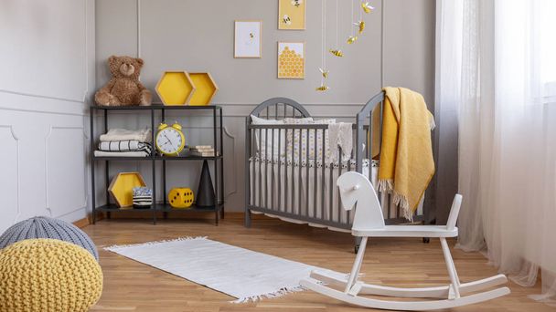 White rocking horse in elegant grey and yellow baby room with industrial shelf and wooden cradle - Zdjęcie, obraz