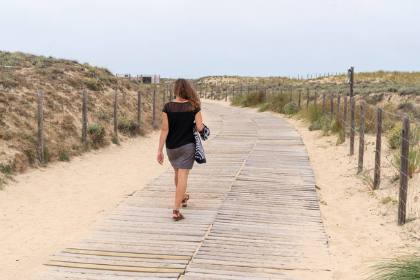 Woman walking on the sandy beach rear view in path wooden - Photo, Image