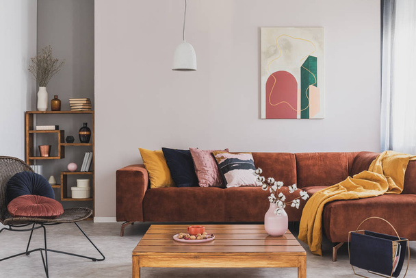 Flowers in vase on wooden coffee table in fashionable living room interior with brown corner sofa with pillows and abstract painting on the wall - Fotó, kép