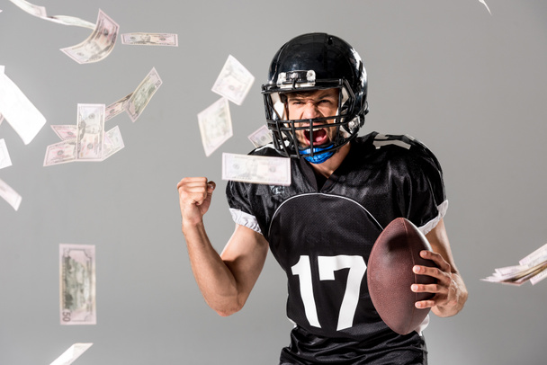 podekscytowany amerykański piłkarz z piłką na szaro z opadającymi pieniędzmi - Zdjęcie, obraz