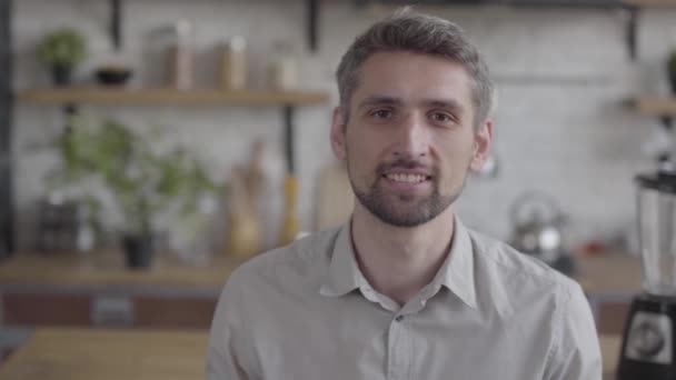 Portrait of a handsome bearded guy confidently looking at camera enjoying executive lifestyle on the background of a modern kitchen. Real people series - Materiał filmowy, wideo