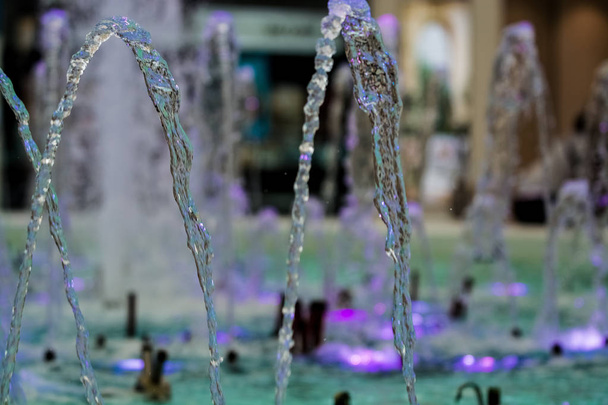 Grandi e forti getti d'acqua dalla fontana con illuminazione blu nel centro commerciale. Schizzi e gocce
. - Foto, immagini