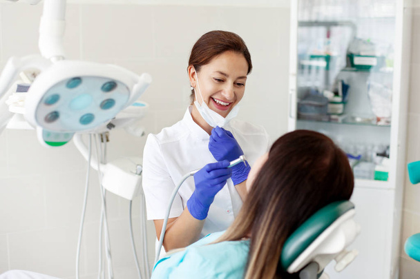 Kobieta dentysta traktuje pacjenta. Kobieta w masce siedzi w fotelu dentystycznym w klinice. Medycyna, zdrowie, koncepcja stomatologii. - Zdjęcie, obraz