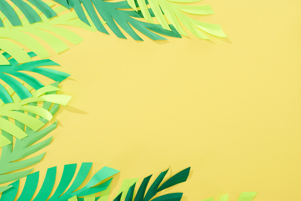top view of paper cut green tropical leaves on yellow bright background with copy space - Fotografie, Obrázek