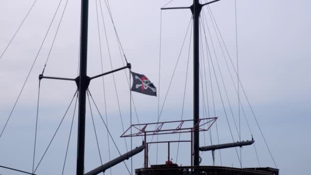 Пиратский флаг Веселый Роджер висит на мачте корабля на голубом фоне неба в ветреный день
. - Кадры, видео