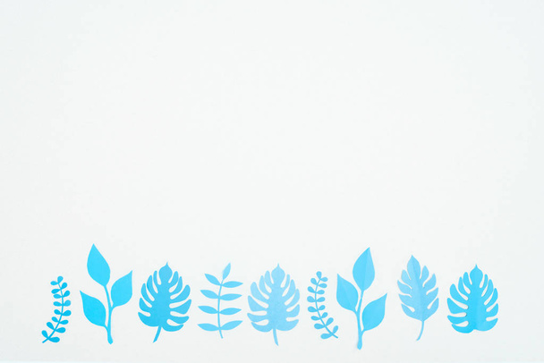 Widok z góry niebieski papier wyciąć tropikalne liście w rzędzie izolowane na białym z kopią przestrzeni - Zdjęcie, obraz