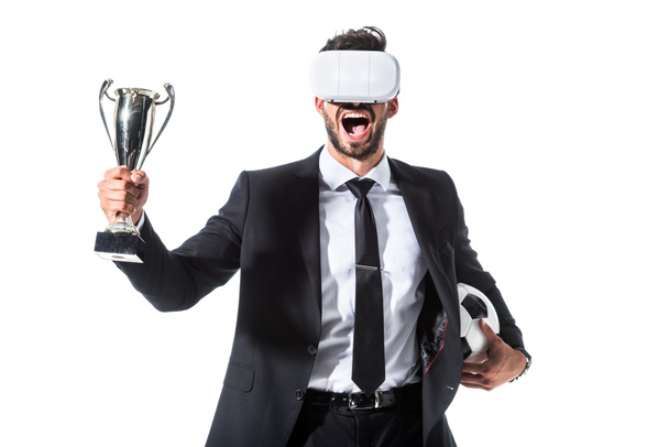 ενθουσιασμένος επιχειρηματίας σε ακουστικά εικονικής πραγματικότητας με μπάλα ποδοσφαίρου και Κύπελλο τρόπαιο απομονωμένη σε λευκό - Φωτογραφία, εικόνα