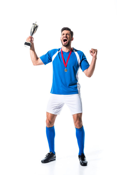 ενθουσιασμένος παίκτης ποδοσφαίρου με Κύπελλο τρόπαιο και μετάλλιο απομονωμένη σε λευκό - Φωτογραφία, εικόνα