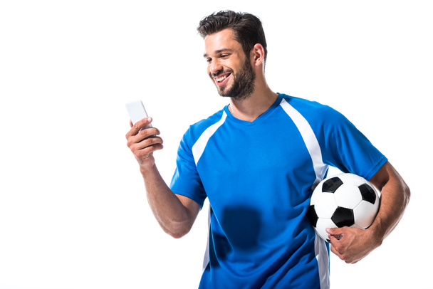 χαμογελαστός παίκτης ποδοσφαίρου με μπάλα χρησιμοποιώντας smartphone απομονωμένη σε λευκό - Φωτογραφία, εικόνα