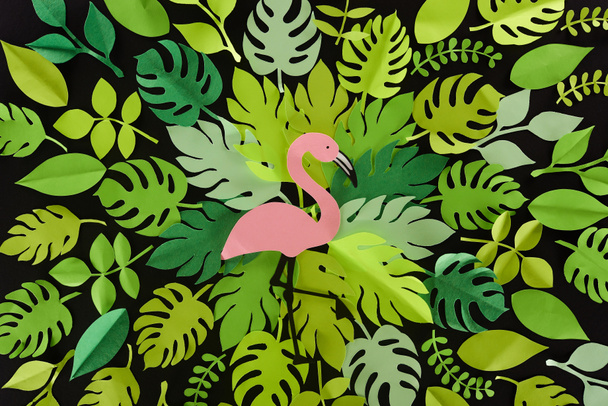 top view of paper cut green leaves with flamingo isolated on black, background pattern - Foto, afbeelding