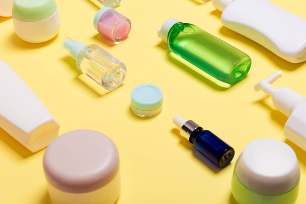 Composition of different sized cosmetic jars and bottles on yellow background. Beauty care concept with copy space - Photo, Image