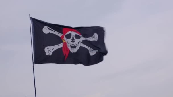 Korsan bayrağı Jolly Roger rüzgarlı bir günde mavi gökyüzü arka plan üzerinde bir gemi direği asılı. - Video, Çekim
