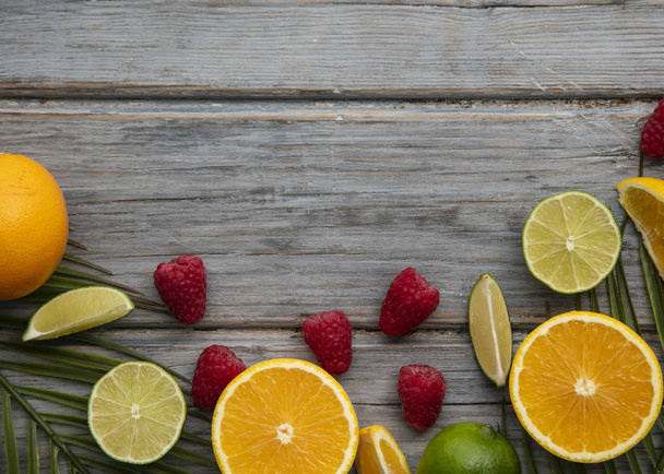 Creative fruits flat lay. Orange, lime and raspberry on the wooden background - Photo, Image