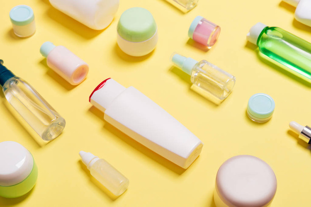 Composition of different sized cosmetic jars and bottles on yellow background. Beauty care concept with copy space - Valokuva, kuva
