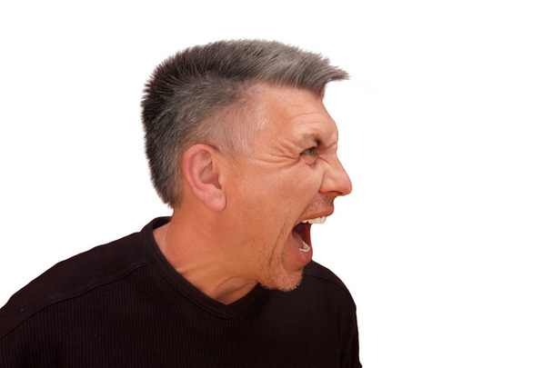 Guy does not look into camera and shouts. Isolated profile portrait on white background. Emotion and gesture of middle aged unshaven shaggy man in black t-shirt. Angry face and aggressive view - Foto, Imagem