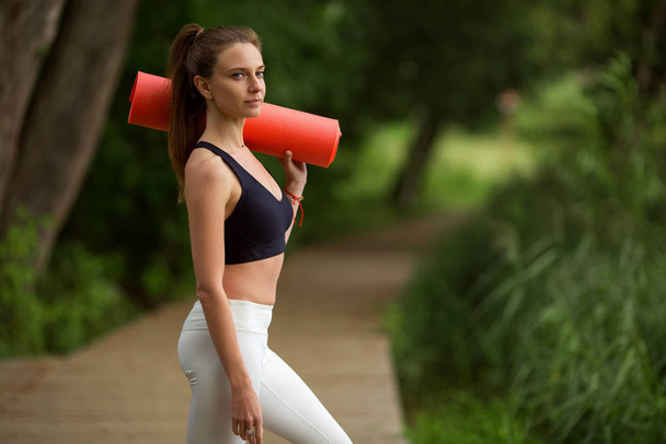 Pretty sportive girl with yoga mat outdoors in green park, summer time - Foto, Imagen