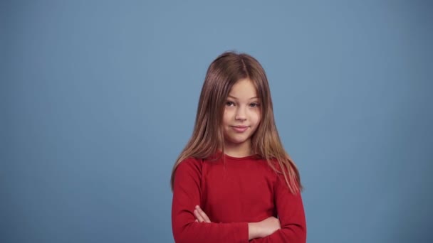 Cute long haired girl in red sweater disapproving with No hand sign, make negation finger gesture. Denying, rejecting, disagree. Portrait of beautiful little girl. Slow motion over blue background - Felvétel, videó