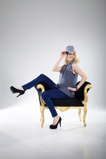 Blonde girl in cap sits in an old chair - Фото, зображення