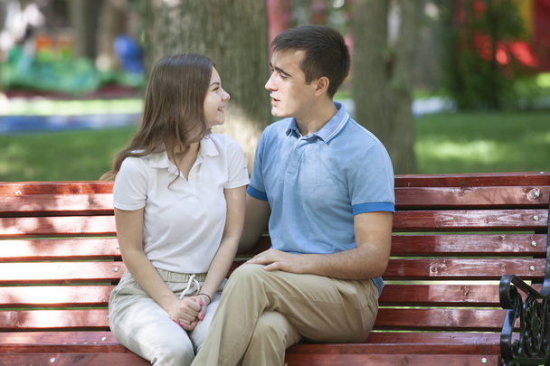 Happy young couple in love sitting on a park bench and looking at camera - Fotó, kép