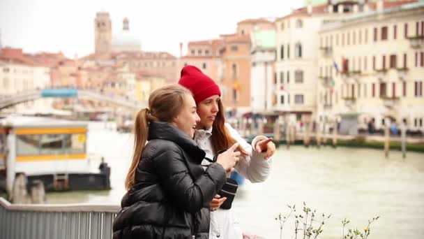Twee jonge vrouwen praten en nemen foto's van de omgeving in de straten van Venetië - Video