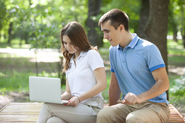 Young couple sitting together on bench in park and using laptop - Foto, Imagem