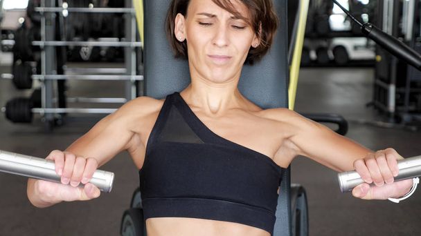 スポーツ女性の初心者は、腕の筋肉のためのシミュレータで初めてワークアウトしています。ジムの新人. - 写真・画像