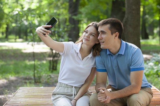 Couple sharing media in a smart phone sitting in a bench in a park. - 写真・画像