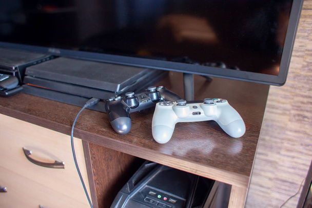 Ζεύγος των joystick από την κονσόλα παιχνιδιού-λαγνεία και λευκό-ξαπλώσετε σε ένα τραπέζι κοντά στην τηλεόραση και την κονσόλα παιχνιδιών - Φωτογραφία, εικόνα