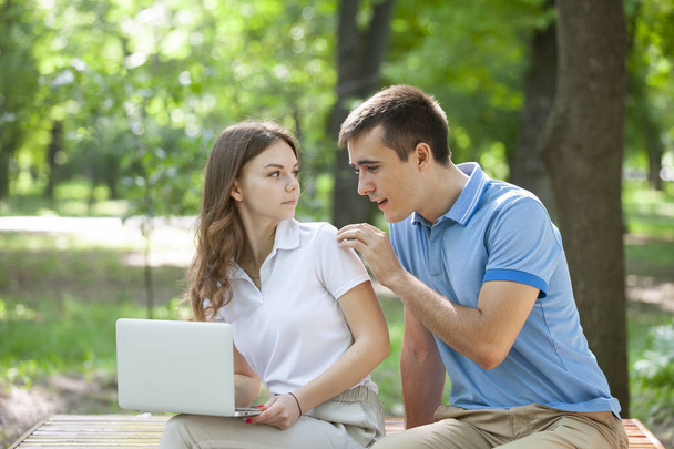 Young couple sitting together on bench in park and using laptop - Фото, зображення