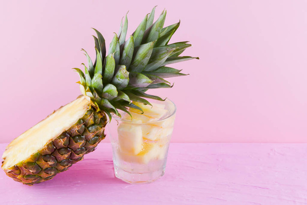 Pineapple and infused water on a pink background. Half of pineapple on a pastel background. Cocktail with pineapple and ice. Minimalism. Copy space - Φωτογραφία, εικόνα