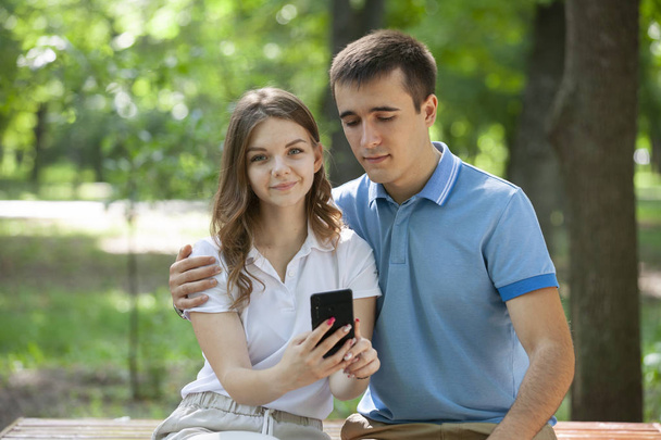 Couple sharing media in a smart phone sitting in a bench in a park. - Foto, imagen