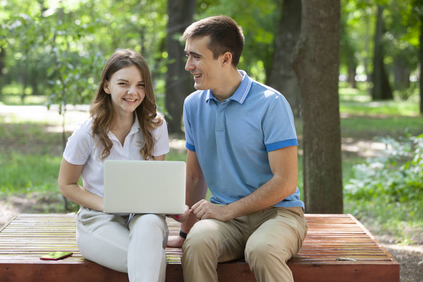 Young couple sitting together on bench in park and using laptop - Foto, immagini